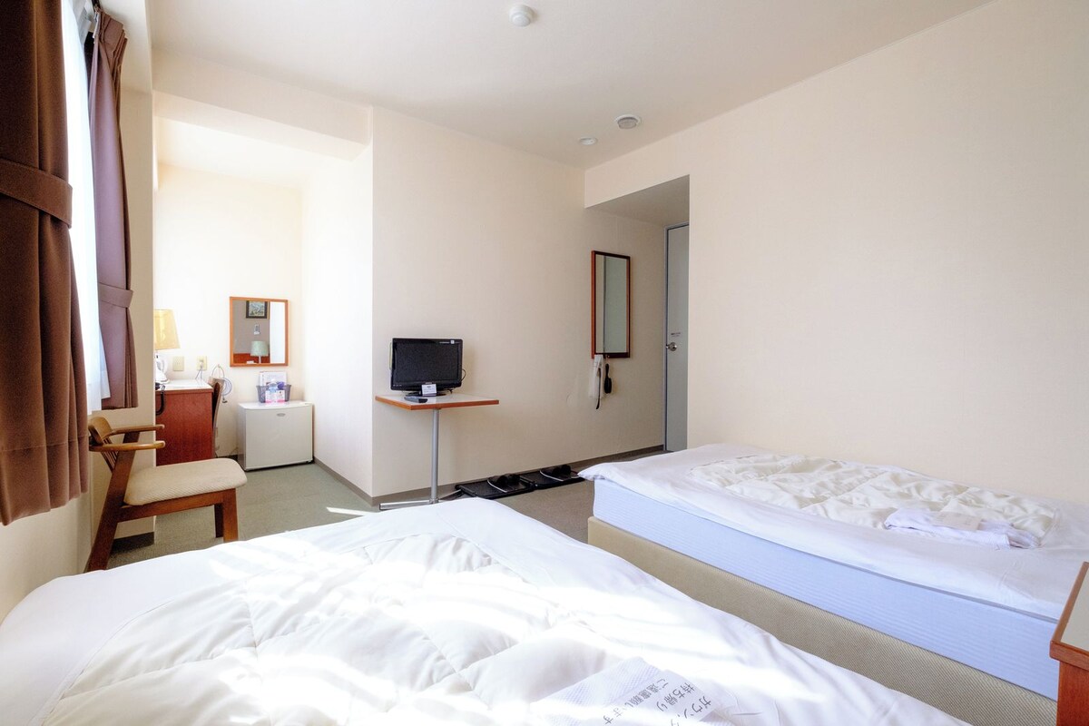 Une chambre d’hôtel avec deux lits, un bureau, une chaise, une télévision et une porte donnant sur une autre pièce.