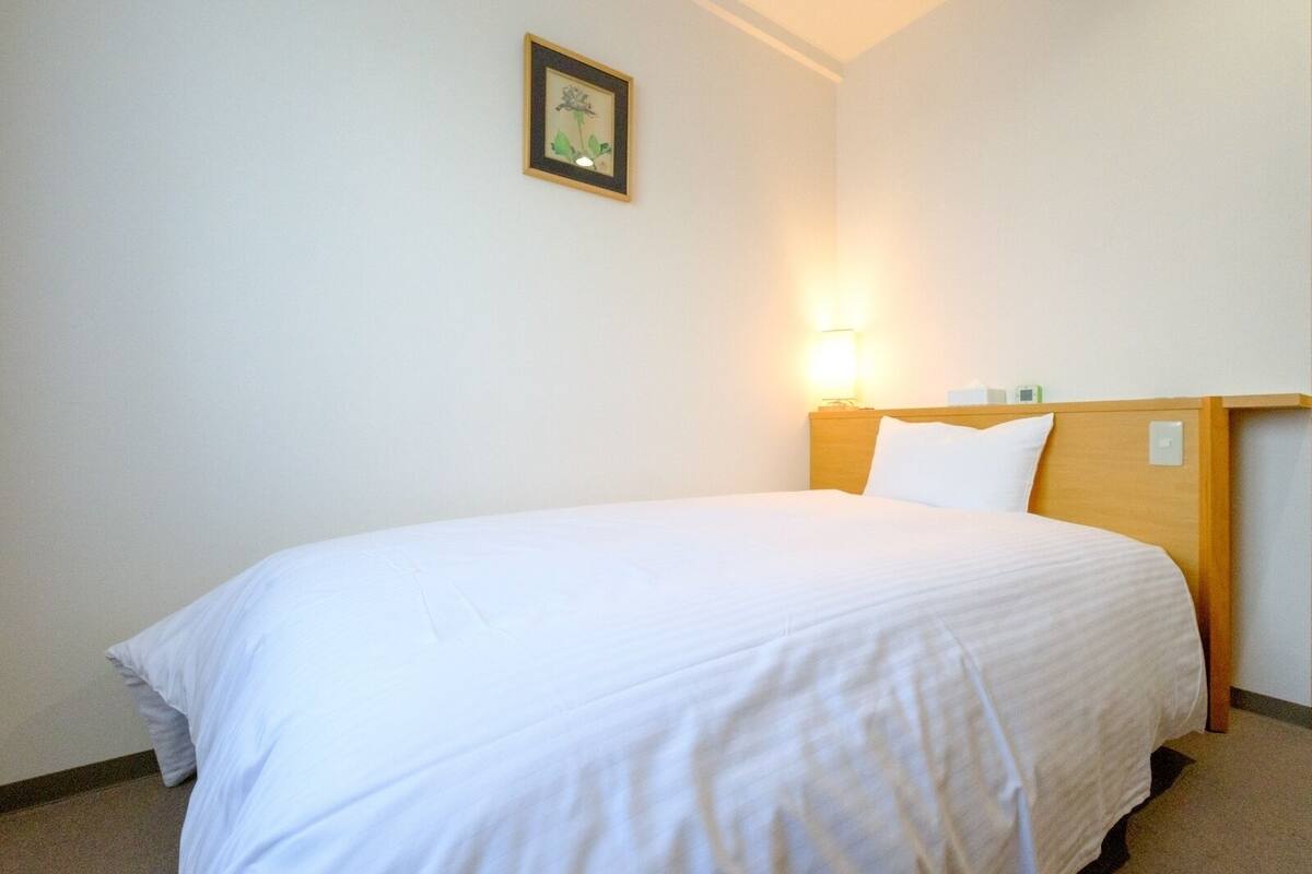 A single bed with a wooden headboard, a bedside table with a lamp, and a framed picture on the wall.