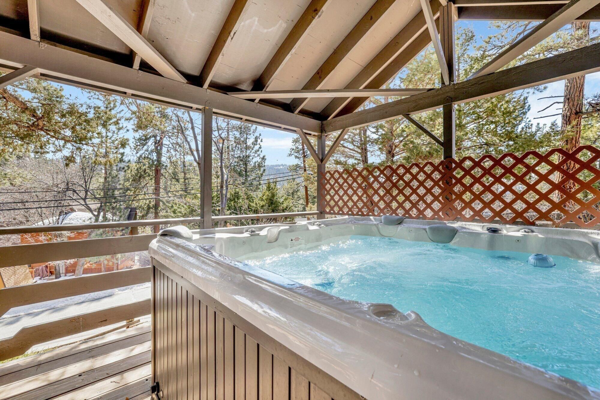 A hot tub under a wooden pergola with a view of trees and a distant landscape.