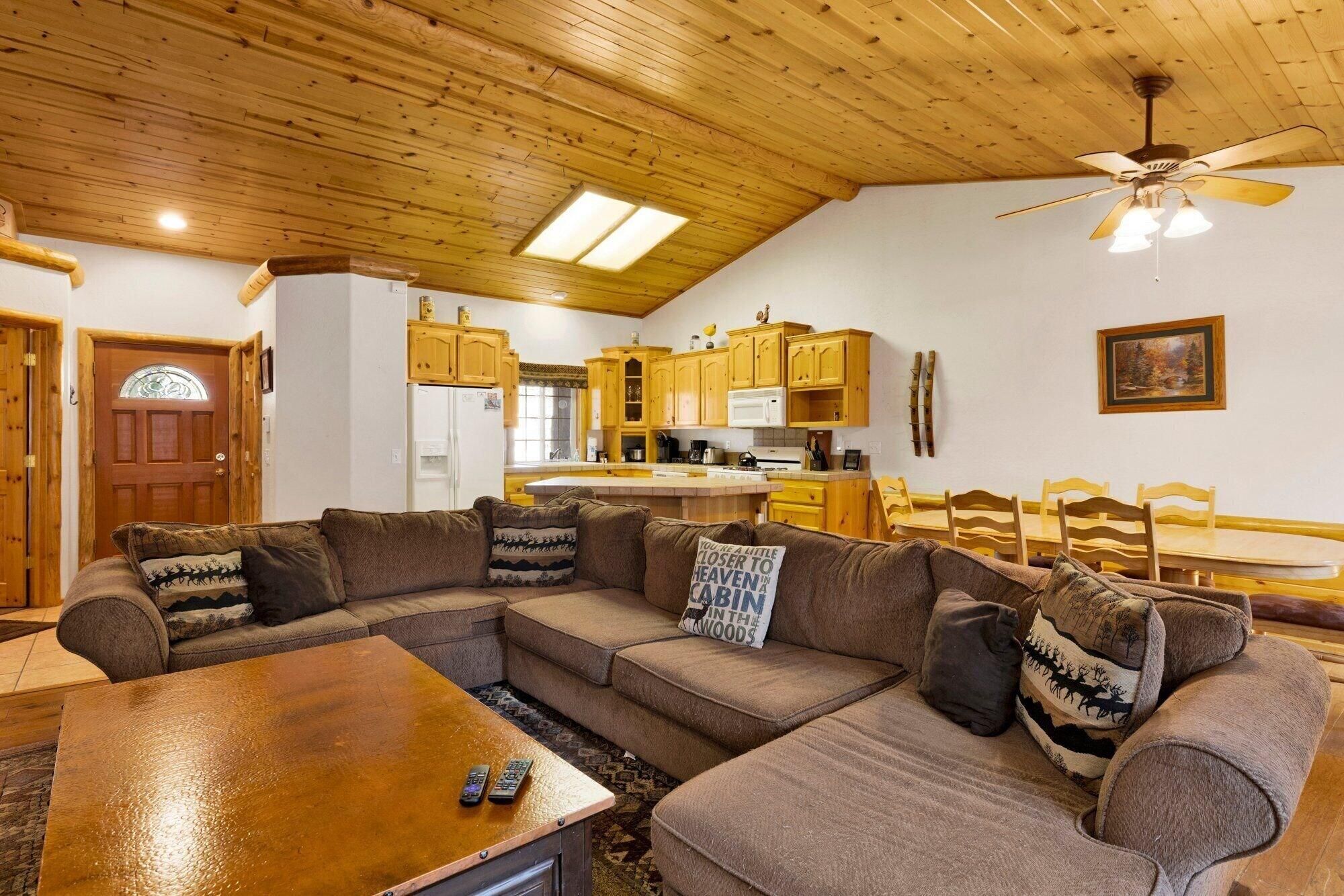 A cozy living room with a sectional sofa, a wooden coffee table, and a ceiling fan.