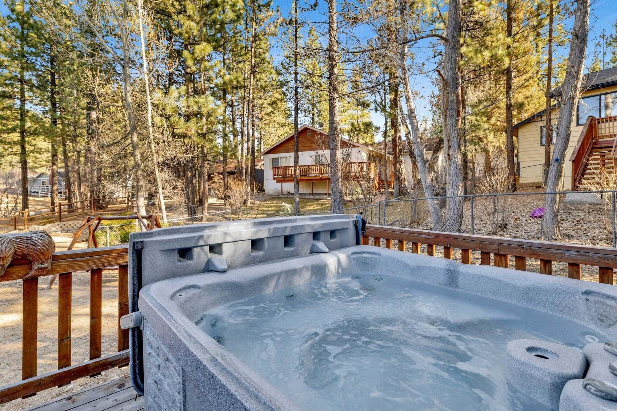 A hot tub on a wooden deck with a view of a house and trees.