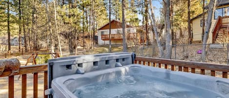A hot tub on a wooden deck with a view of a house and trees.
