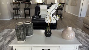 A living room with a white coffee table, three decorative vases, a black leather sofa, and a dining area in the background. - Relaxing 4-bedroom Pool Oasis Near Daytona (Port Orange)