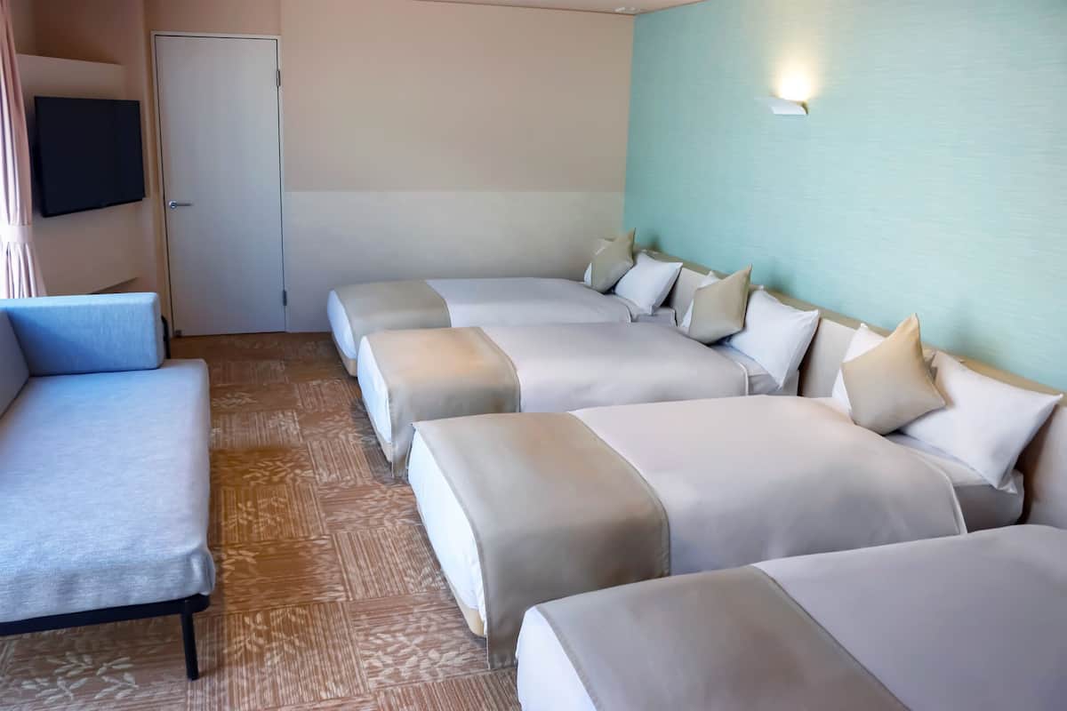 Une chambre d’hôtel avec un canapé, trois lits, un téléviseur à écran plat et un luminaire fixé au mur.