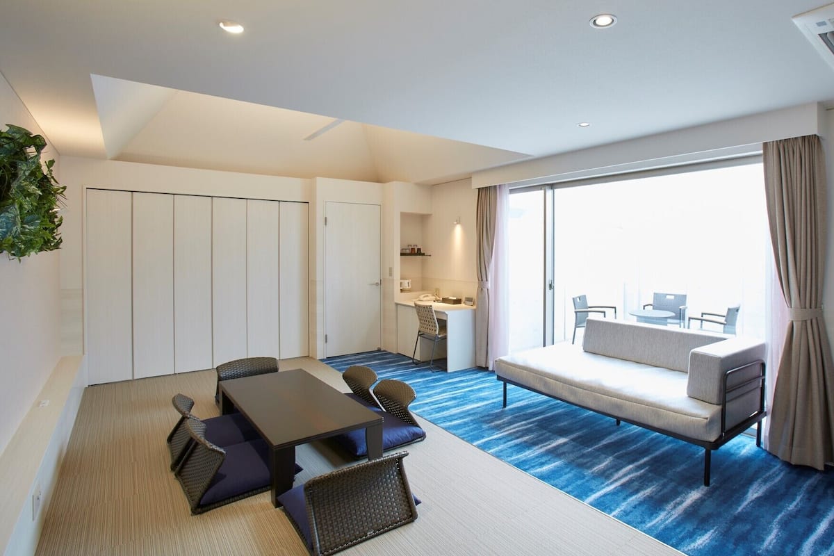 Une chambre d’hôtel moderne dotée d’un coin repas, d’un canapé, d’une télévision et d’une grande fenêtre.