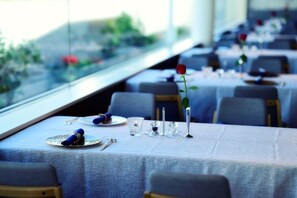 A dining area with tables set for service, a view through a window, and a rose on one table. - Blanchette Nanki Shirahama (Shirahama)