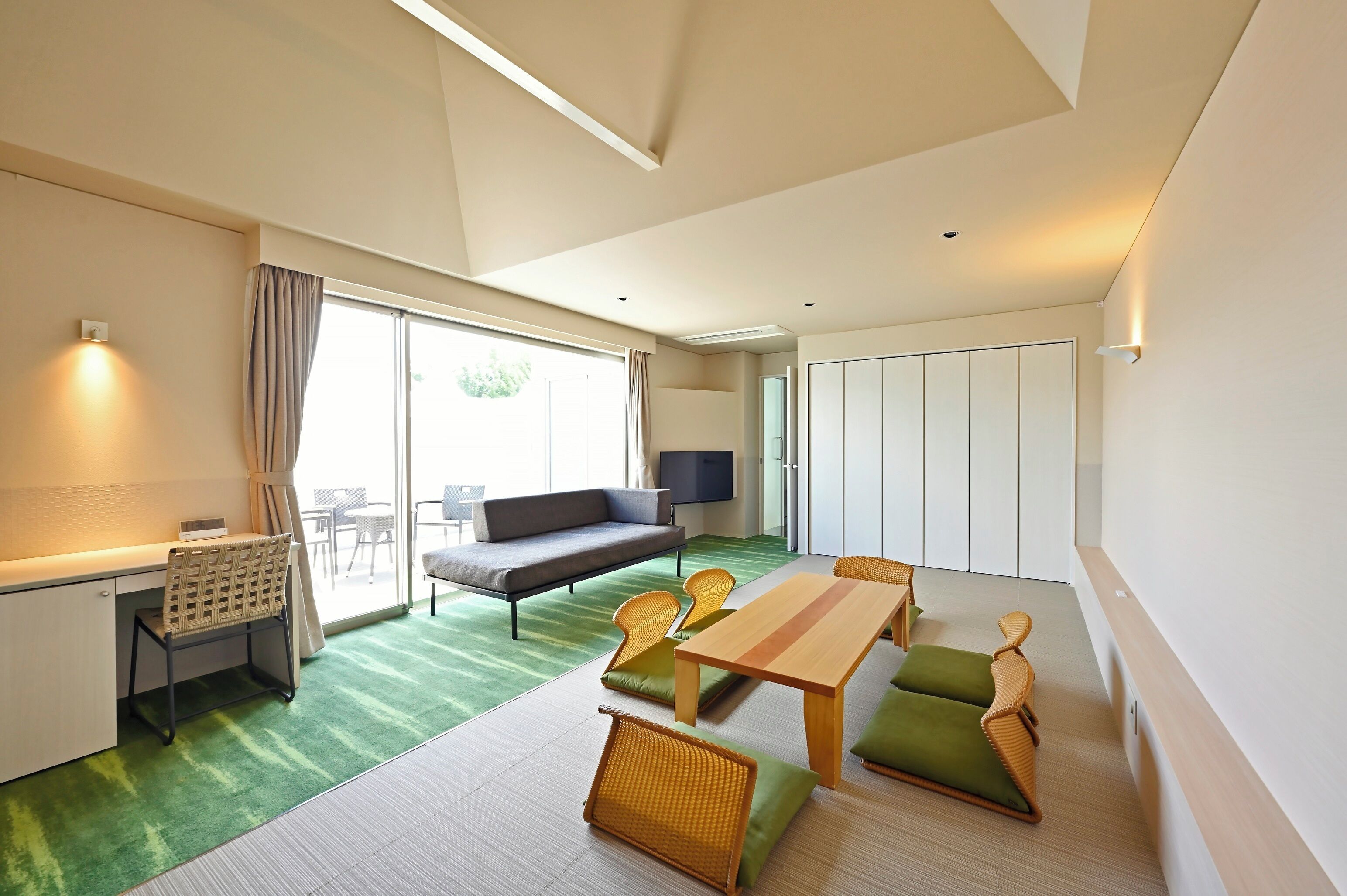 A modern hotel room with a sofa, dining table, chairs, a desk, and a TV.