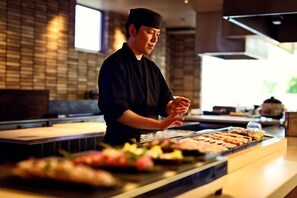 A sushi bar with a chef preparing food, a counter with various dishes, and a brick wall in the background. - Blanchette Nanki Shirahama (Shirahama)