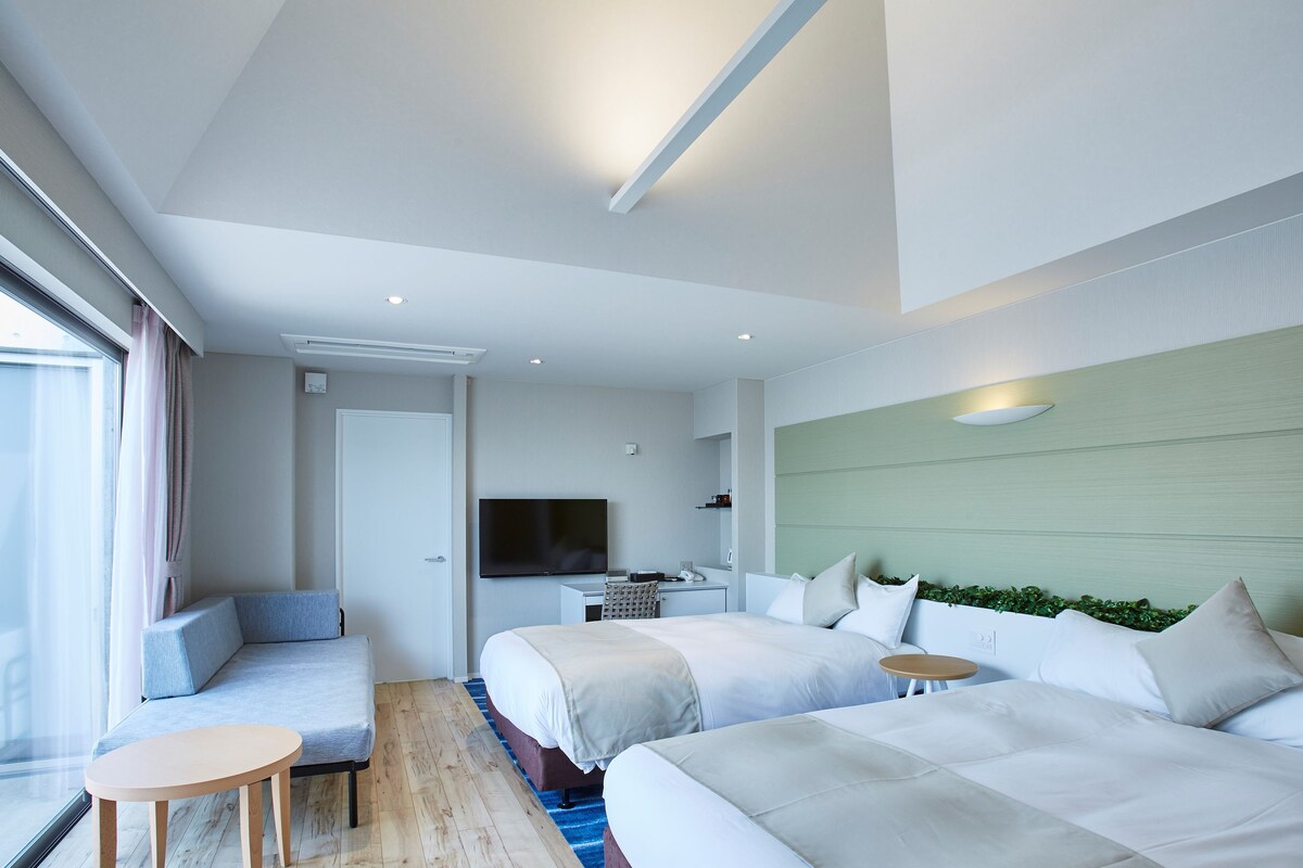 A modern hotel room with a large bed, a smaller bed, a TV, a desk, and a seating area.