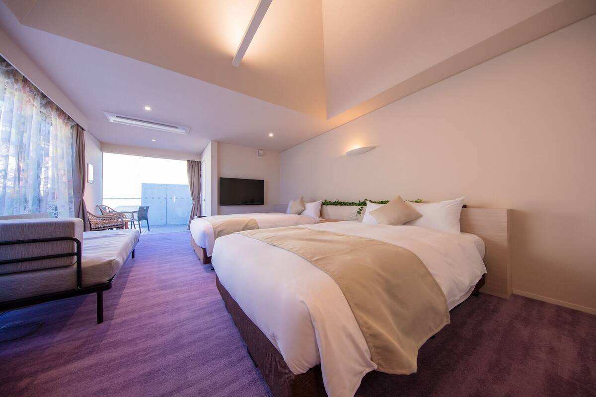 Une chambre d’hôtel avec deux lits, une télévision, un coin salon avec des fauteuils et une vue par la fenêtre.