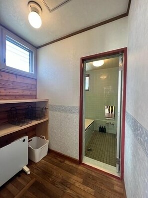 A compact bathroom with a wooden vanity, a window, and a shower area visible through a glass door. - Albergo Del Otto (Fujikawaguchiko)
