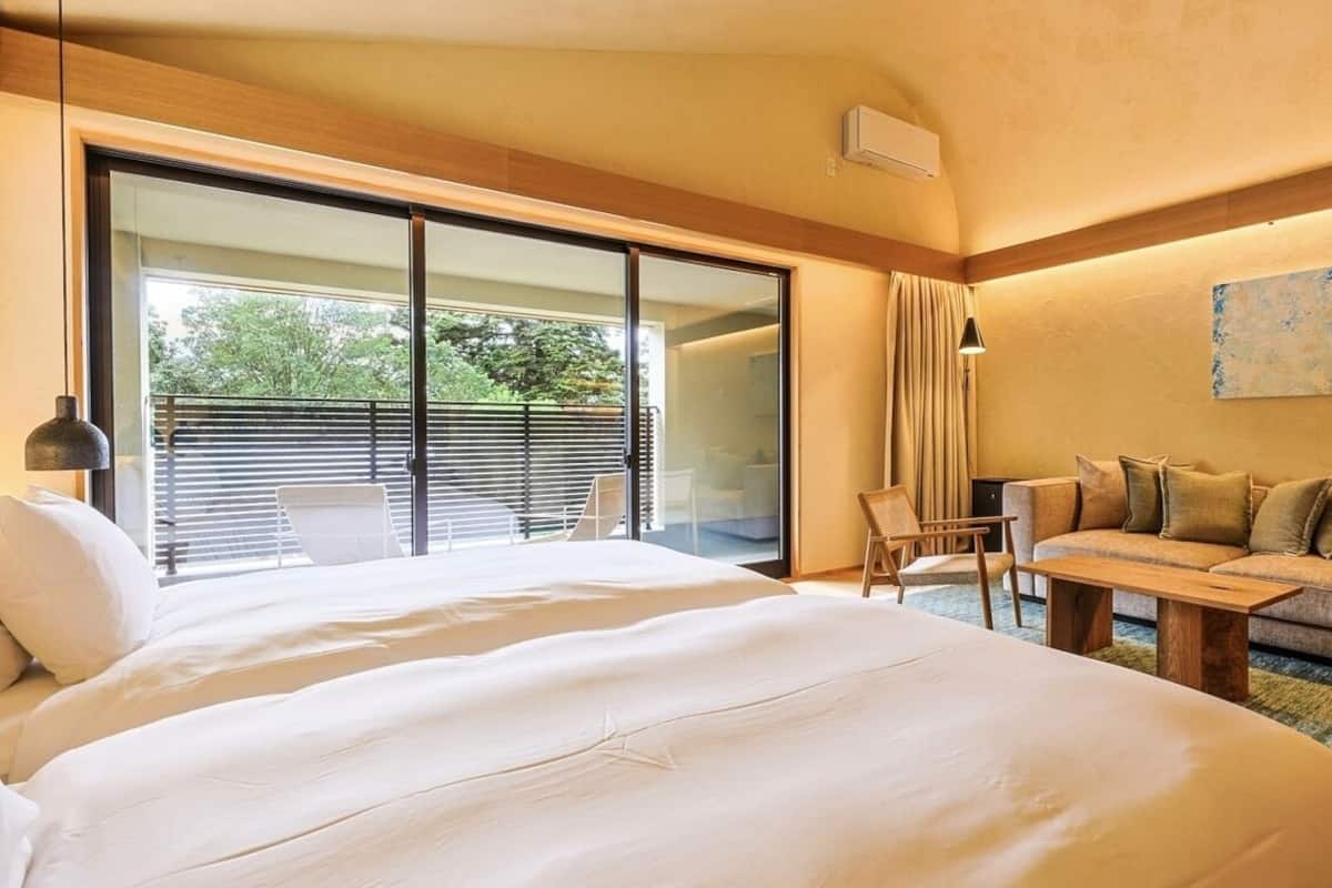 Une chambre d’hôtel avec un grand lit, un canapé, une petite table et une porte-fenêtre coulissante donnant sur un balcon.
