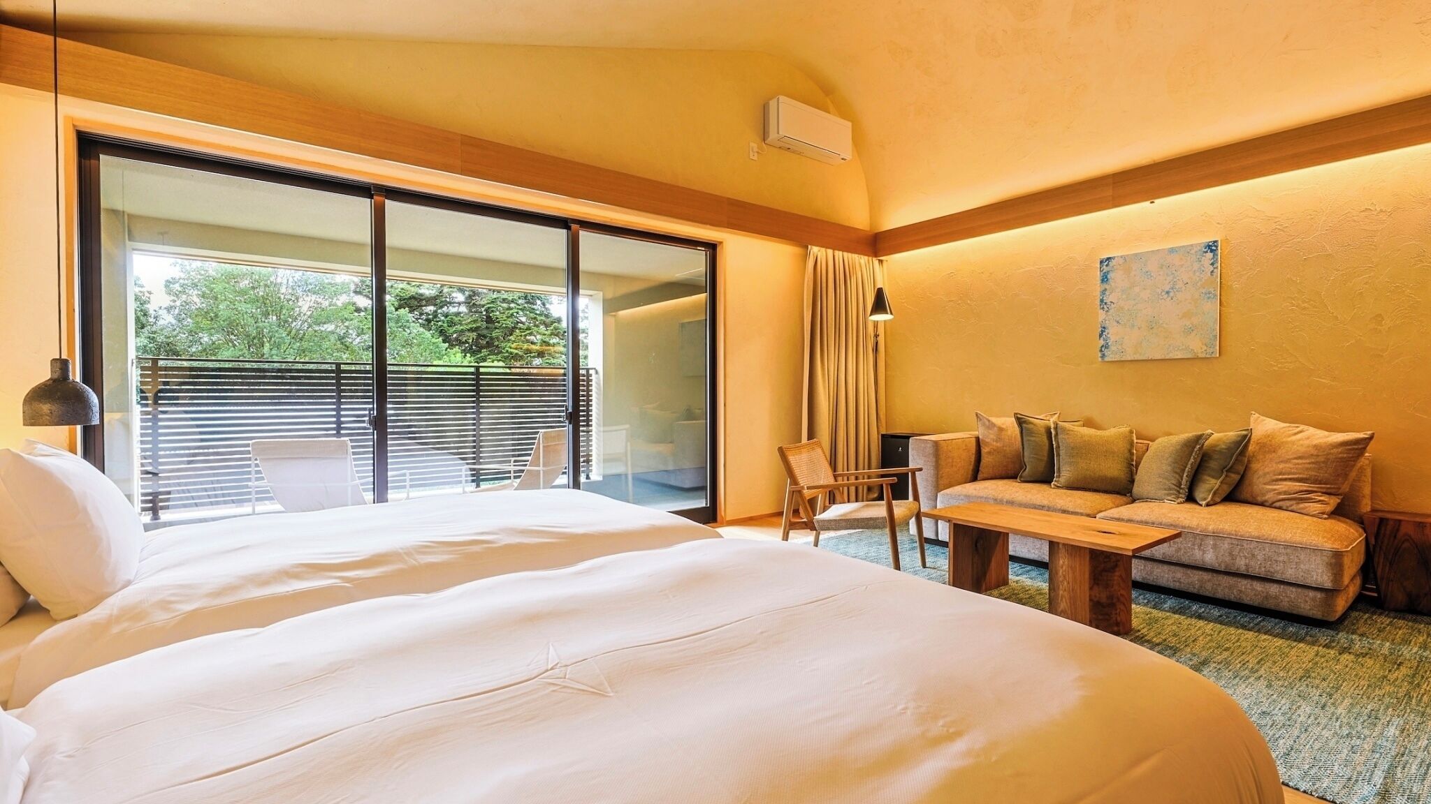 Camera d'albergo con un letto grande, un divano, un tavolo da pranzo, una sedia, una porta scorrevole in vetro su un balcone e un quadro appeso al muro.