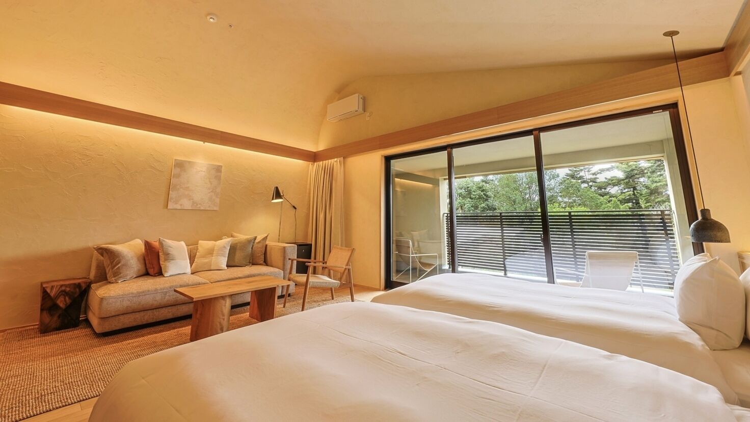A hotel room with a large bed, a sofa, a chair, a desk, and a sliding glass door to the outside.