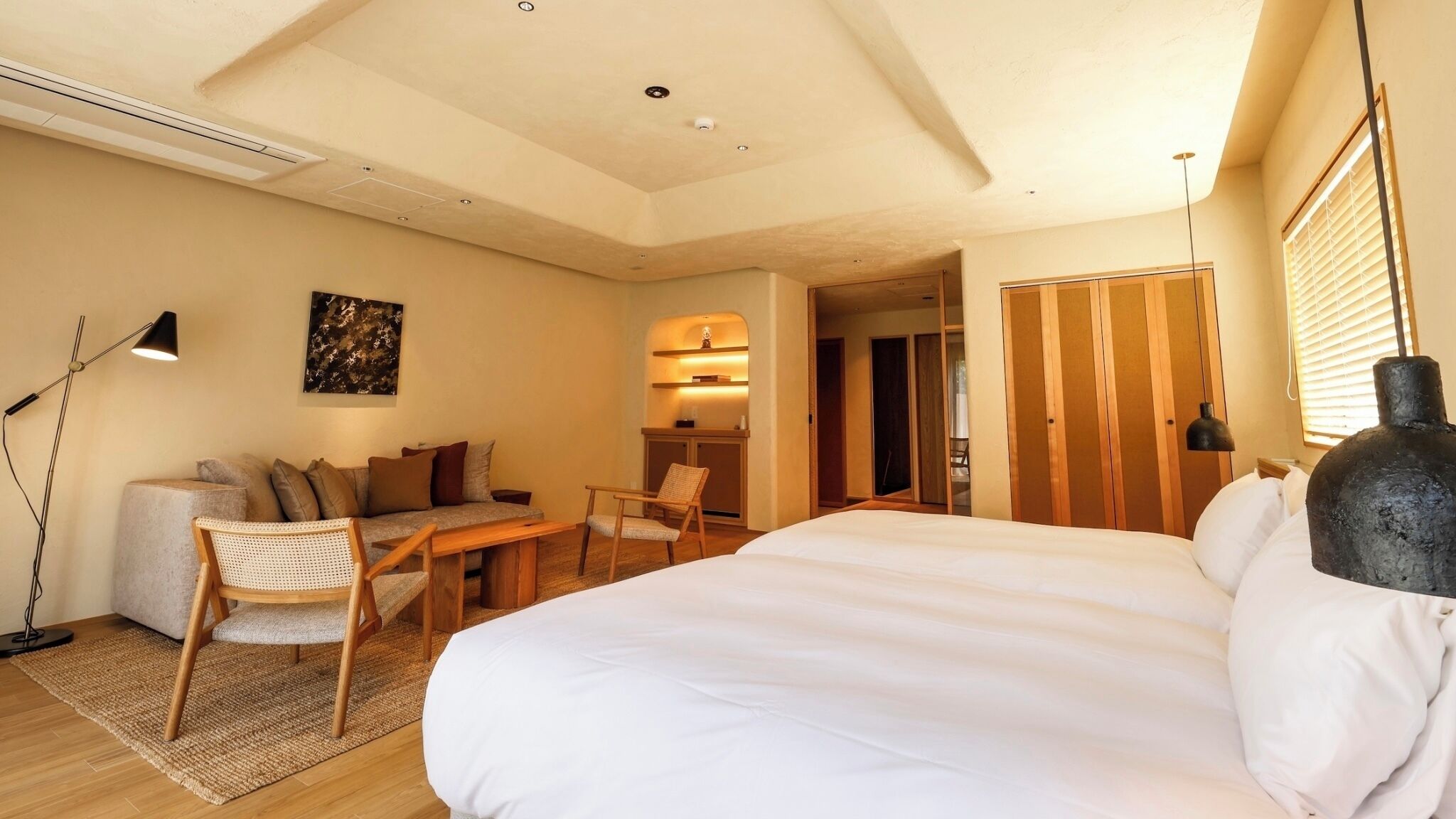 Camera d'hotel con un letto, una poltrona, una scrivania, una sedia, una lampada e un armadio.