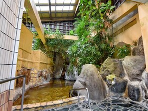 Un site de sources chaudes doté d’une piscine en pierre, de murs recouverts de carreaux et d’une végétation luxuriante.