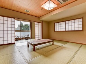 Une pièce de style japonais traditionnel, avec un sol recouvert de tatamis, une petite table en bois, des portes coulissantes en papier de riz (shoji) et une vue dégagée sur l’extérieur grâce à une grande fenêtre.