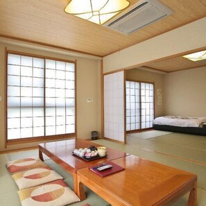 Ein traditioneller japanischer Raum mit Tatami-Böden, Schiebetüren, einem Holztisch mit Kissen und einem Bett mit Futon.