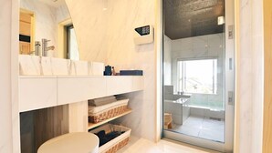 Un baño moderno con tocador de mármol, cabina de ducha de vidrio y vistas al exterior.