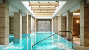 Une piscine intérieure moderne, dotée d’une eau claire, d’une échelle en métal et d’une cascade décorative.