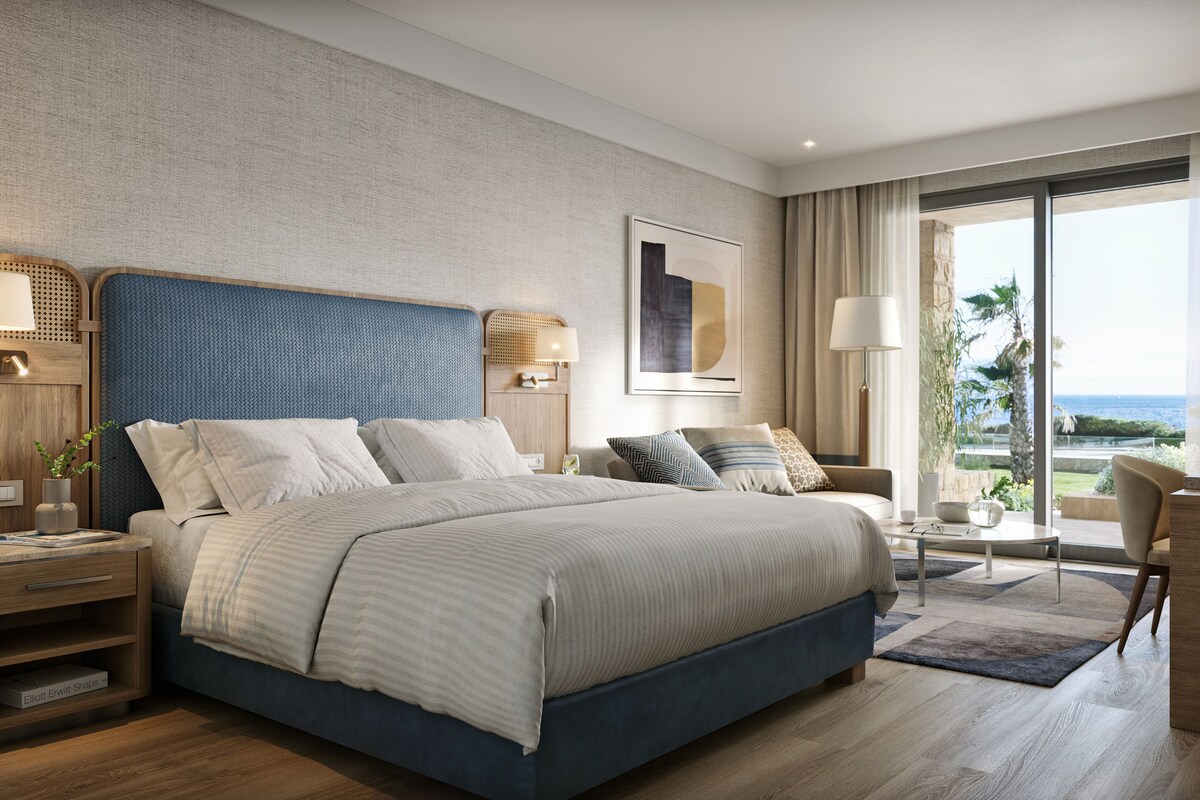 A modern hotel room with a large bed, a desk, and a view of the ocean.