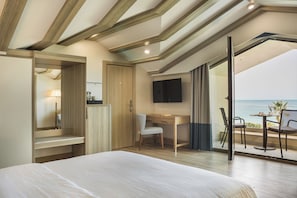 A bedroom with a bed, a desk, a chair, a TV, and a balcony with a view of the sea. - Electra Kefalonia Hotel and Spa (Kefalonia)