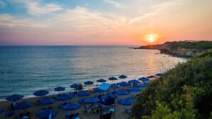 Une plage avec des parasols et des chaises, un coucher de soleil et une côte rocheuse.