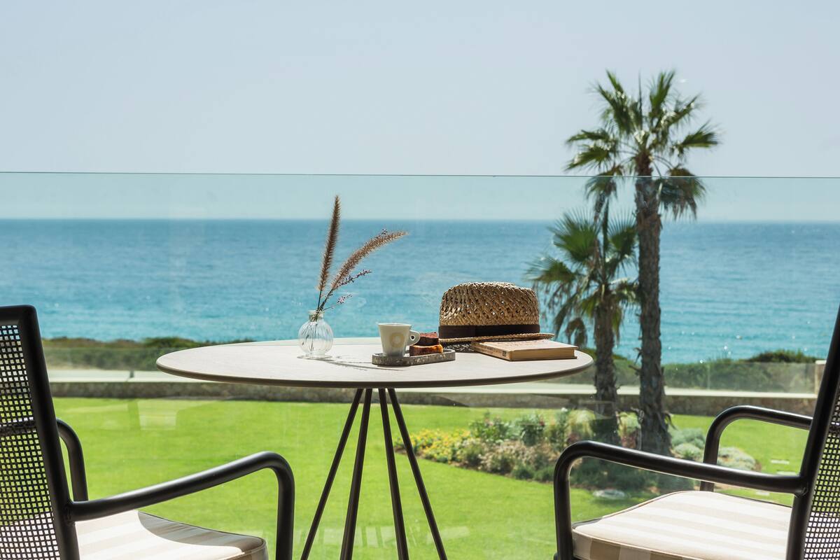 A round table with a vase, a cup, and a basket on a balcony overlooking the ocean.