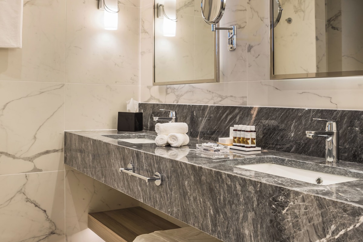 A modern bathroom with a marble vanity, a large mirror, and built-in shelves for towels.