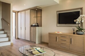 Una sala de estar moderna con una mesa de centro de vidrio, un televisor de pantalla plana montado en la pared y un mueble de madera con cajones.