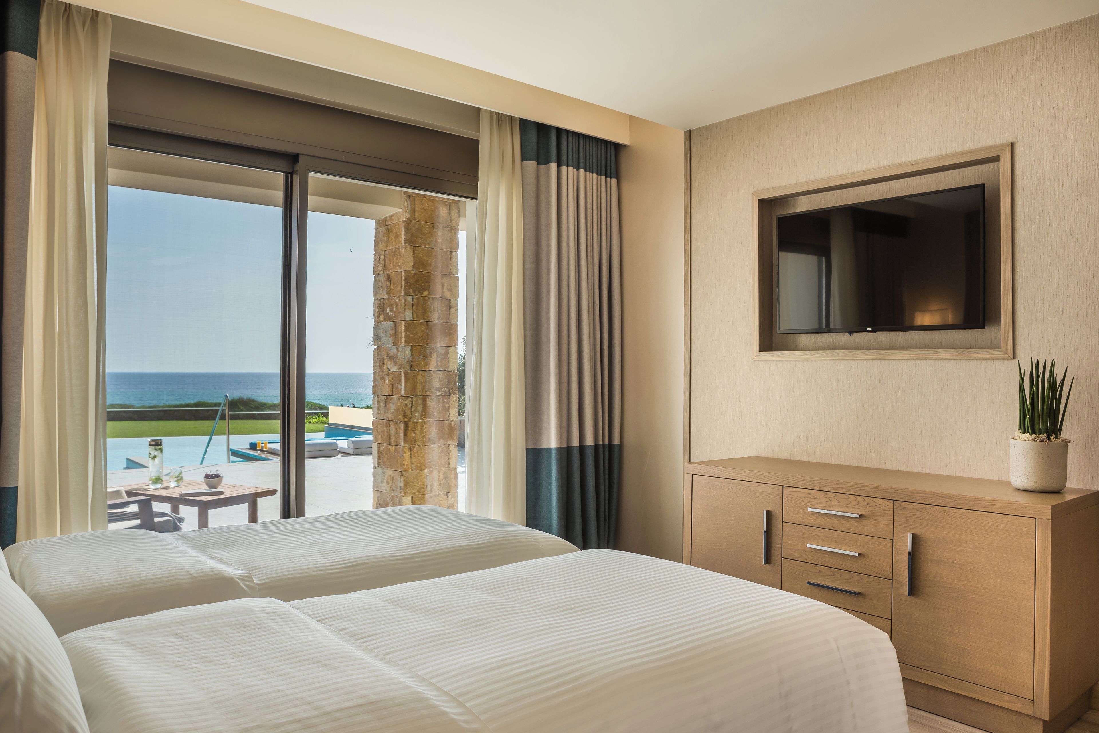 A hotel room with two beds, a TV, a wooden cabinet, and a view of the ocean.