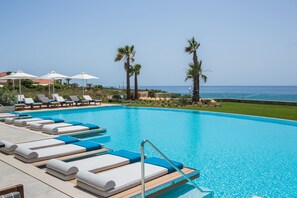 A pool with lounge chairs and umbrellas, palm trees, and a view of the ocean. - Electra Kefalonia Hotel and Spa (Kefalonia)