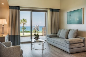 Un salón moderno con sofá, sillón y mesa de centro, vista al océano y un cuadro en la pared.