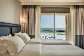 Habitación de hotel con una cama grande, una mesita de noche, una lámpara y vista al océano.