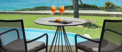 A poolside table with two glasses of orange beverage, a plate of food, and a view of the ocean.
