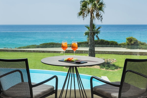 Una mesa junto a la piscina con dos vasos de bebida de naranja, un plato de comida y vista al océano.