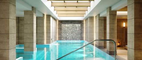Una piscina interior moderna con agua cristalina, una escalera metálica y una cascada.