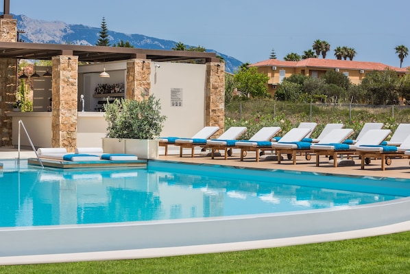 Una piscina con sillones reclinables, un bar y vistas a las montañas.