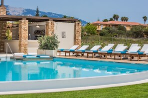 A pool with lounge chairs, a bar area, and a view of mountains.