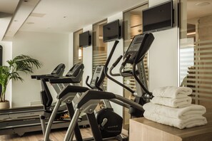 Ein Fitnessraum mit Laufbändern, einem Ergometer und einem an der Wand befestigten Fernseher.