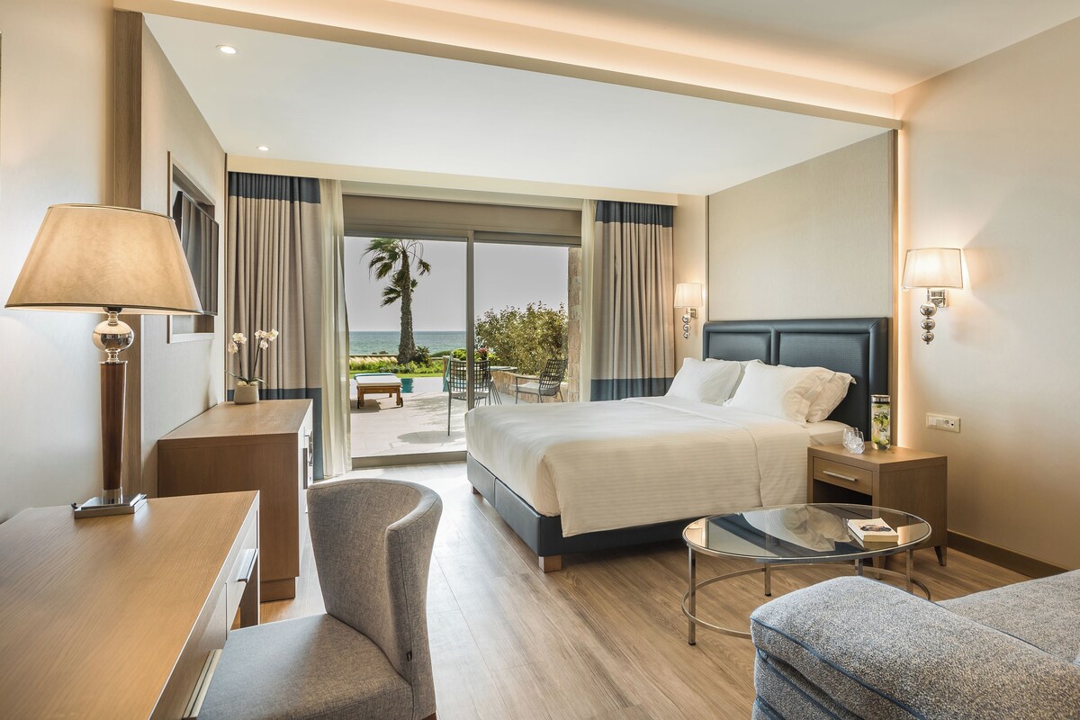 A hotel room with a bed, a desk, a chair, a small table, and a view of the outdoors.