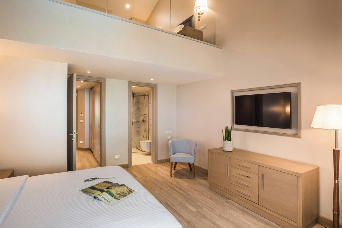 A hotel room with a bed, a TV, a chair, a cabinet, and a bathroom visible through an open door.