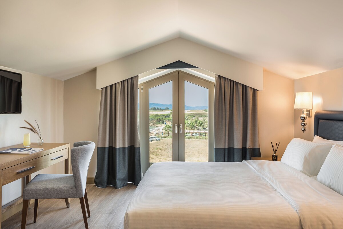 A hotel room with a bed, desk, chair, and a large window with curtains.