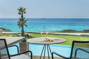 A poolside table with two glasses of wine, a plate of food, and a view of the ocean. - Electra Kefalonia Hotel and Spa (Kefalonia)