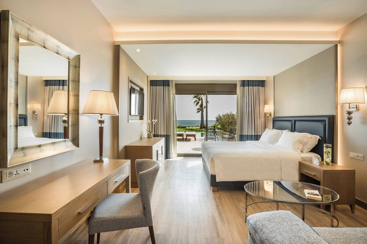 A hotel room with a bed, desk, chair, and a glass table.