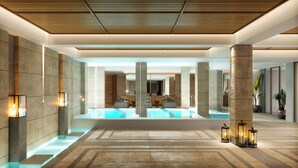 Un hall d’hôtel moderne doté d’une piscine centrale, de colonnes en pierre et d’un éclairage d’ambiance.