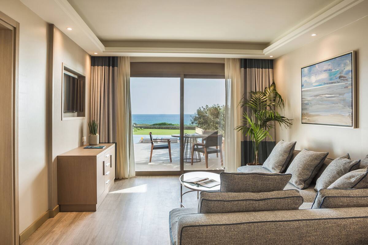 A modern living room with a sofa, a coffee table, and a view of the ocean through large sliding doors.