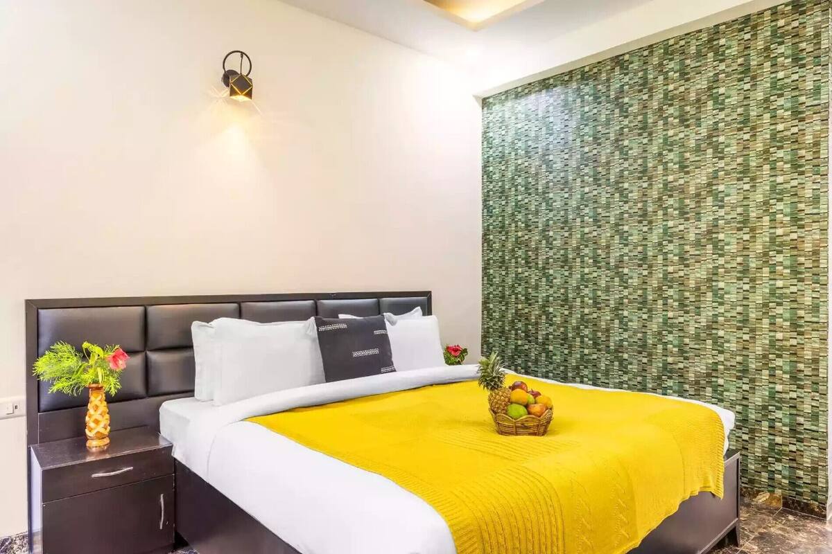 A hotel room with a bed, a nightstand, a vase with flowers, and a wall with a green textured pattern.