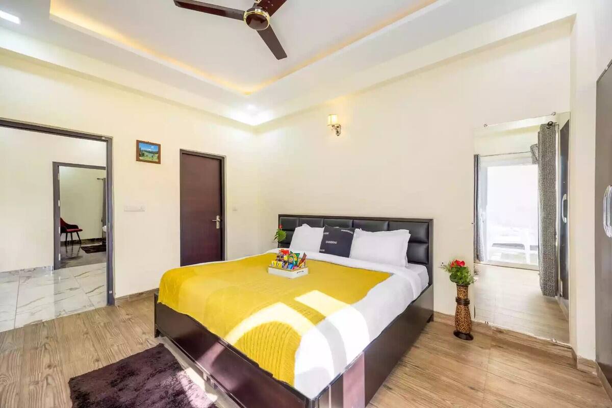 A bedroom with a bed, a ceiling fan, a bedside table with a plant, and a window with curtains.
