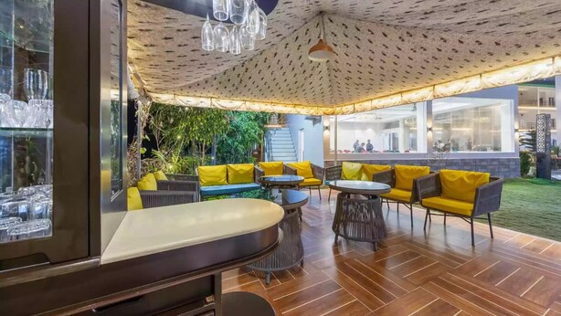 An outdoor seating area with yellow cushions, a wooden floor, and a patterned ceiling. - Alaya Stays By Elivaas Kingdom Heartz (Nainital)